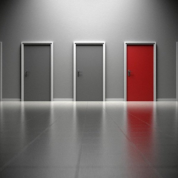 a series of dimly lit gray doors with one red door